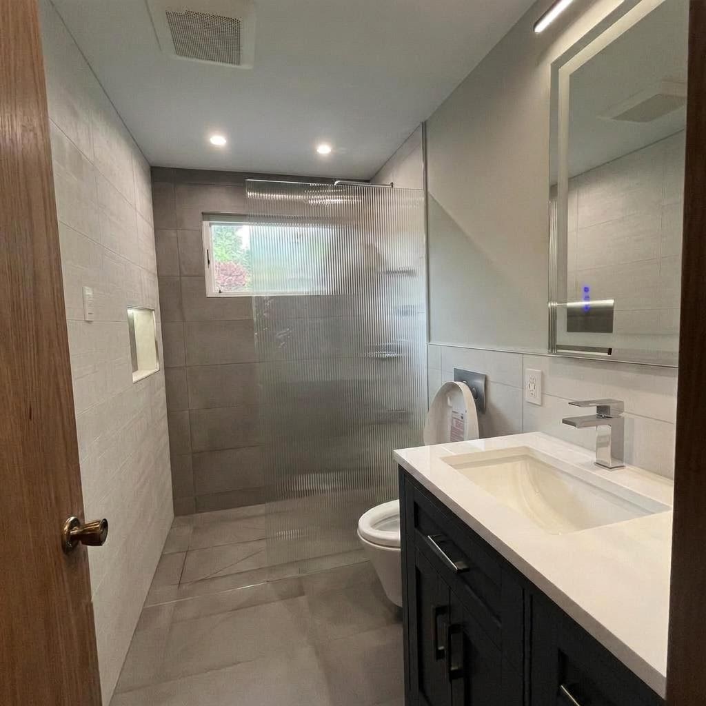 Bathroom after full remodel — frameless glass shower, grey tile, black vanity